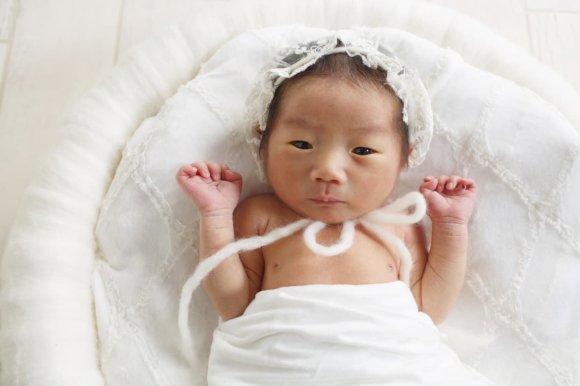 カメラ目線で白い布に包まれた赤ちゃん